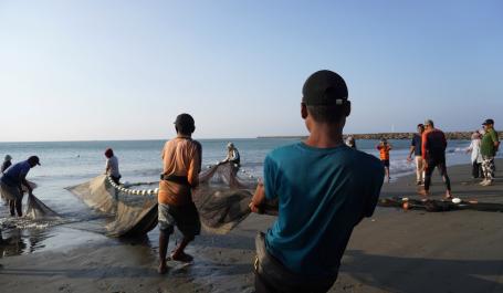 Fishermen in Indonesia haul in their nets on a beach.