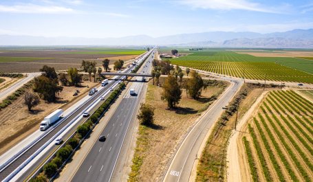 Cars drive down a California highway with farm fields on either side.