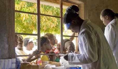 Health workers in Kenya prepare supplies in front of a window with children looking through on the other side.