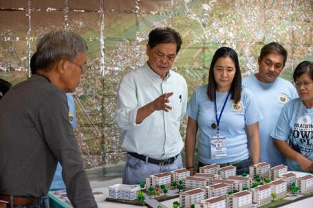Members of Iloilo City government and community organizations stand around a table of a model housing development.
