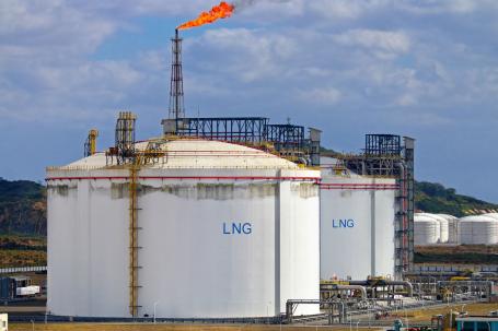 A gas flare flames from the top of a large white tank storing liquified natural gas.