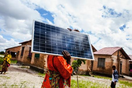 Woman carrying solar panel to be installed on new housing in Africa