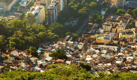 An aerial view of a cluster of small homes next to luxury buildings, all surrounded by trees.