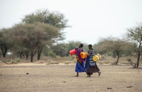 Two women carry water cannisters on their way to a well in Tanzania.
